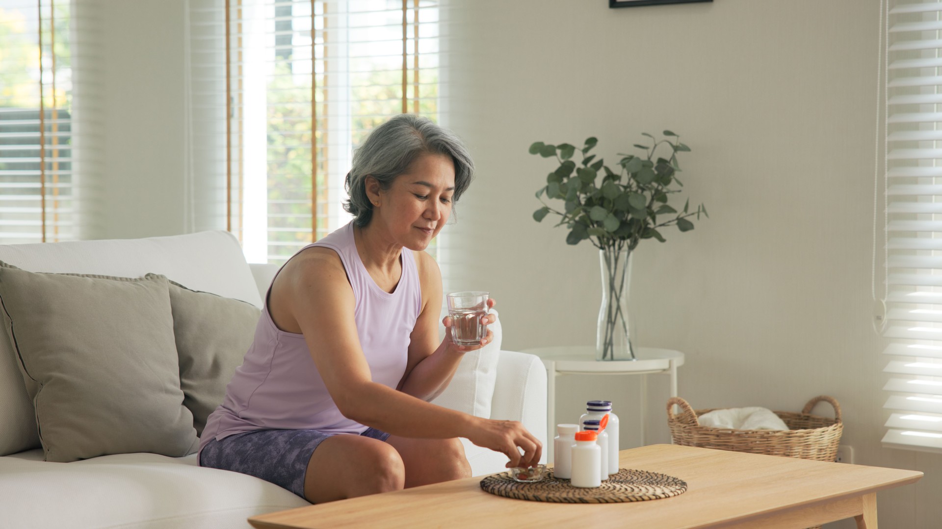 Asia adult aged people middle age happy old woman smile drink vitamin d c e k zinc omega 3 fish oil water pill reduce hot flash dry skin health care sit at home sofa elder aging asian. Take diet food.